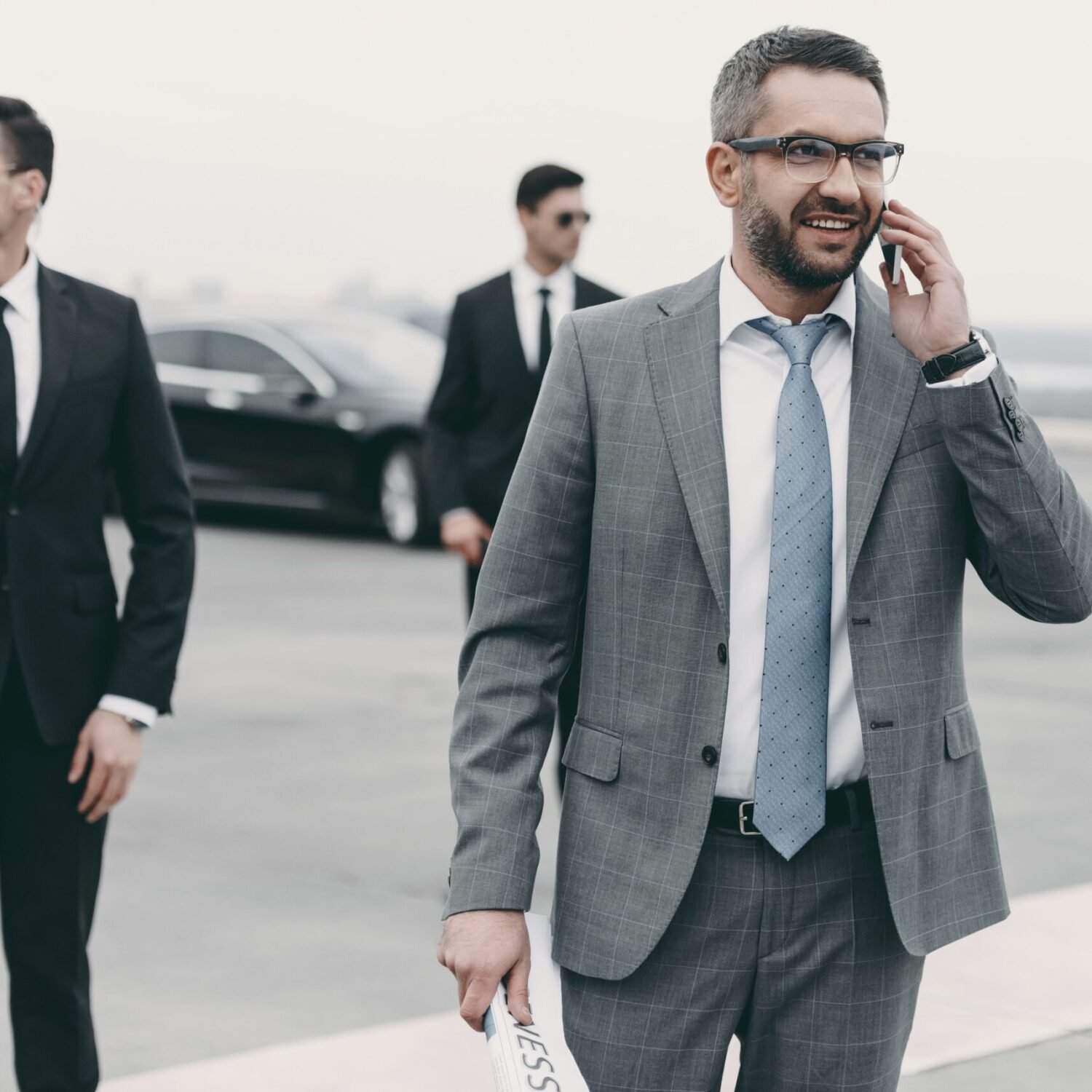 smiling-businessman-walking-with-bodyguards-and-ta-P6JESYF-min